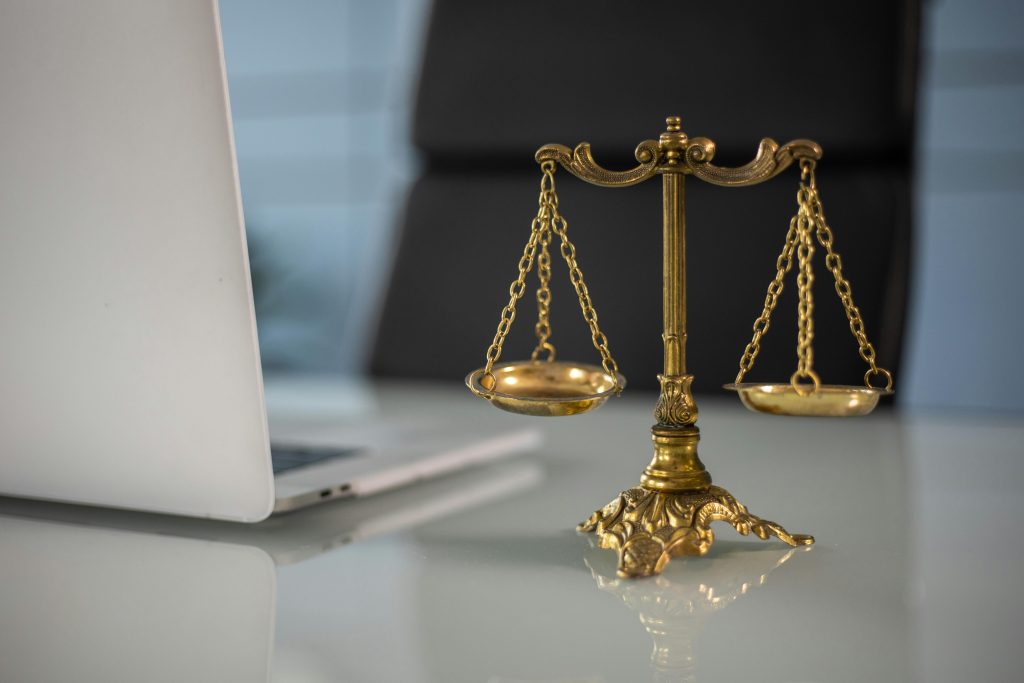 Golden justice scales on a desk beside a laptop, symbolizing law and balance.Debate