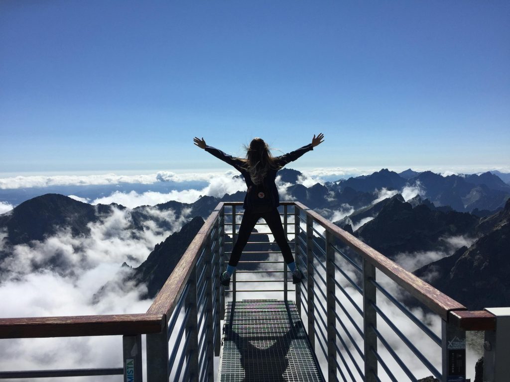A woman stands on a viewing platform in Vysoké Tatry, Slovakia, surrounded by clouds and mountains, embracing freedom.Life tricks
