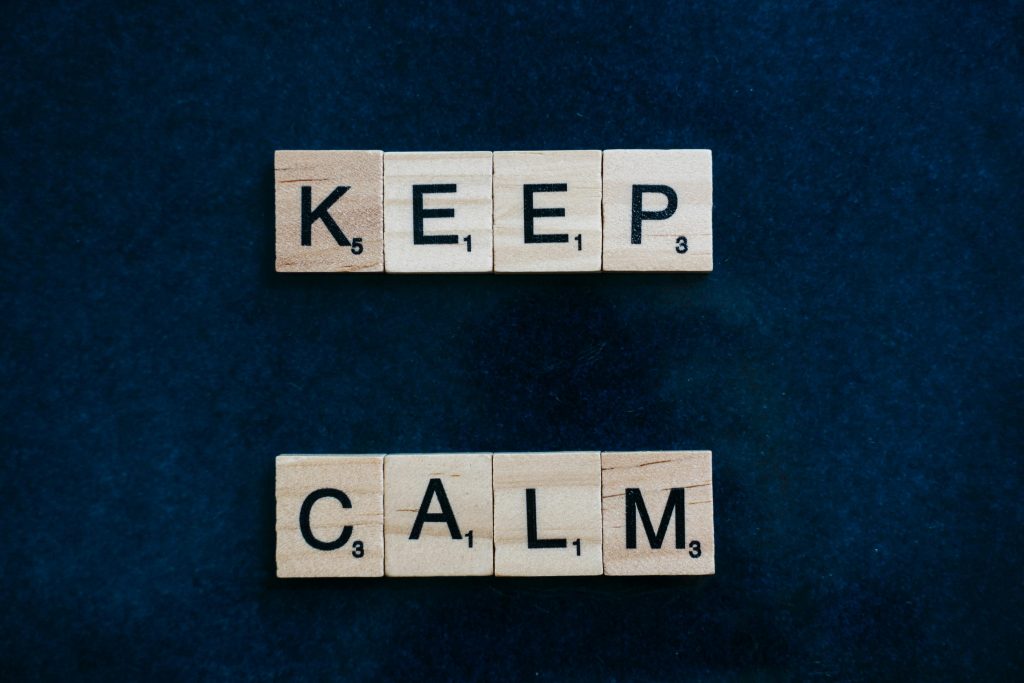 Scrabble tiles spelling 'Keep Calm' on a blue surface, viewed from above. English Sentence Making